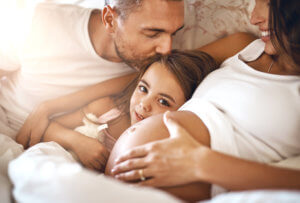 Shot of a happy little girl lying in bed with her dad and pregnant mother